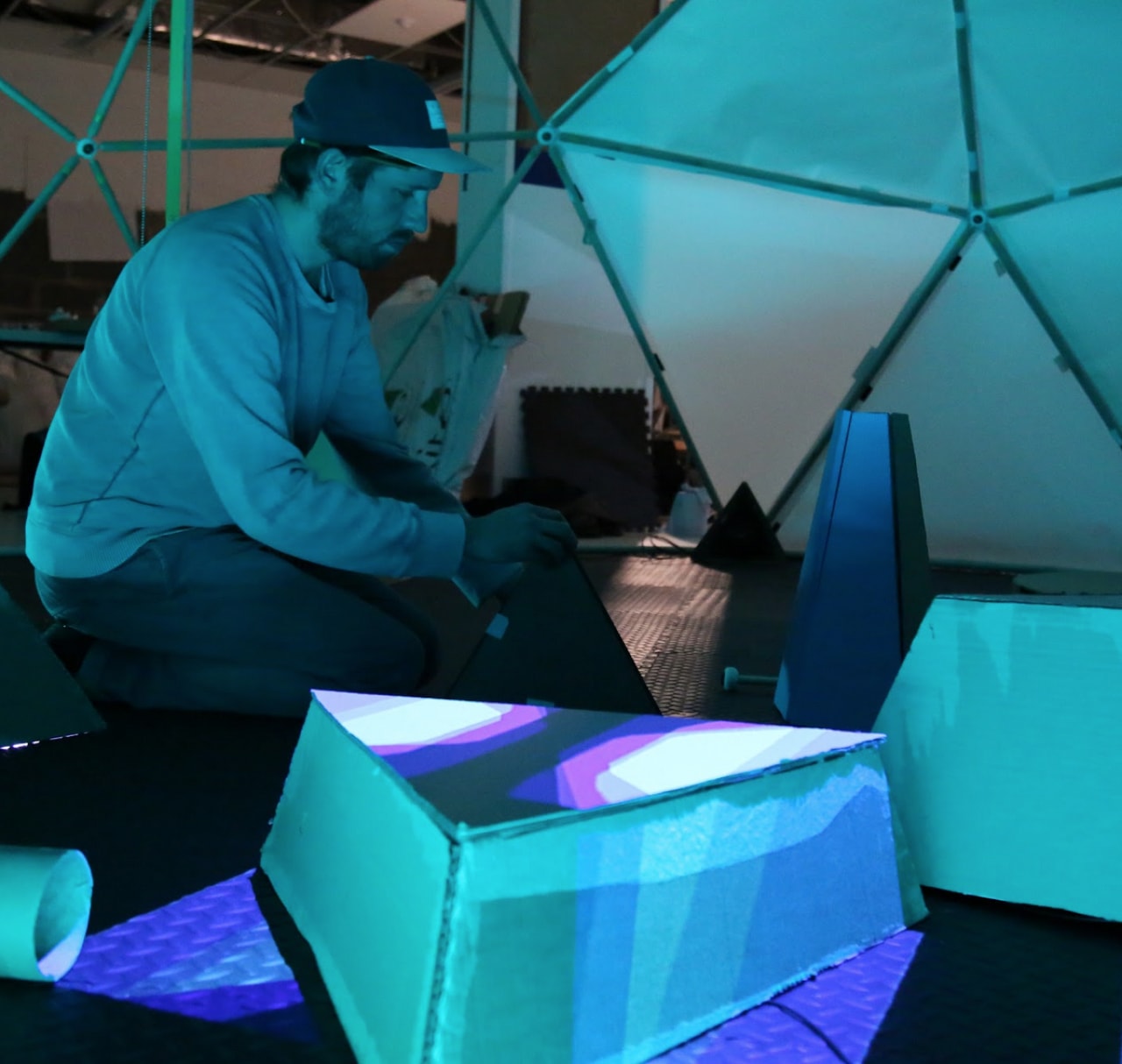 A man folds together an instrument inside a geometric dome lit with a blue lighting