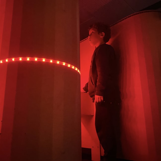 A kid stands inside a structure with red LED lights in front of them arranged into a circle