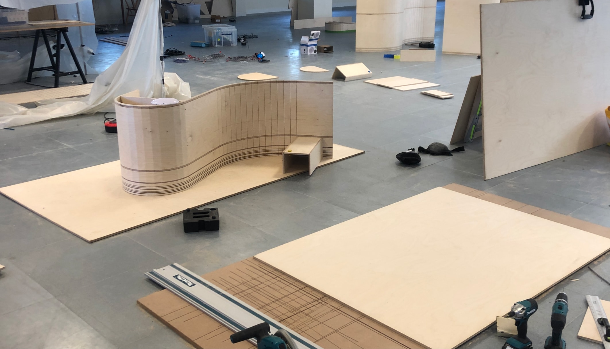 Wood panels are laid out over a floor with one upright folded into the shape of a curve