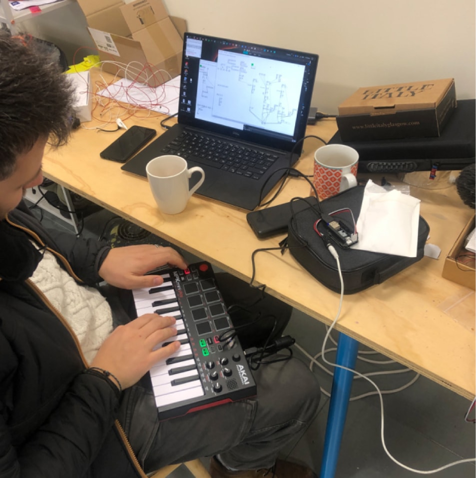A teenager plays a keyboard connected to a computed sitting on a desk in front of them